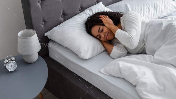 Stressed black woman covering ears lying in bed