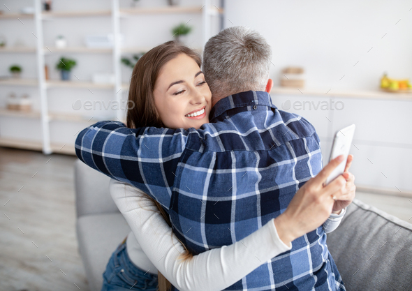 Gadget addiction or infidelity. Mature woman hugging husband, stuck in smartphone, playing online