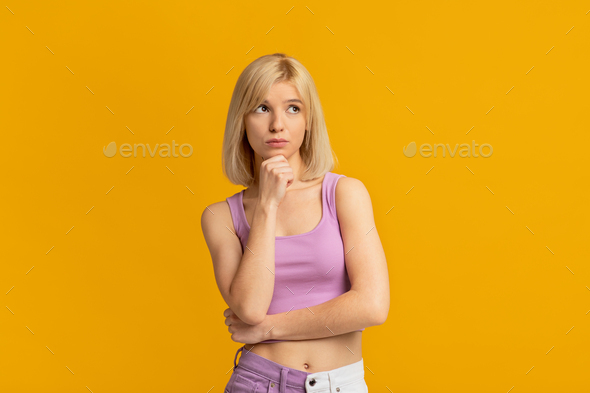 Let me think. Doubtful woman thinking about offer or proposal and touching chin, yellow background