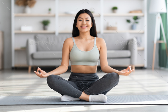 Happy young chinese woman sitting yoga pose and watching