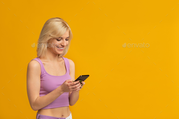 Cool gadget. Excited lady using smartphone, browsing internet or chatting in social networks, yellow