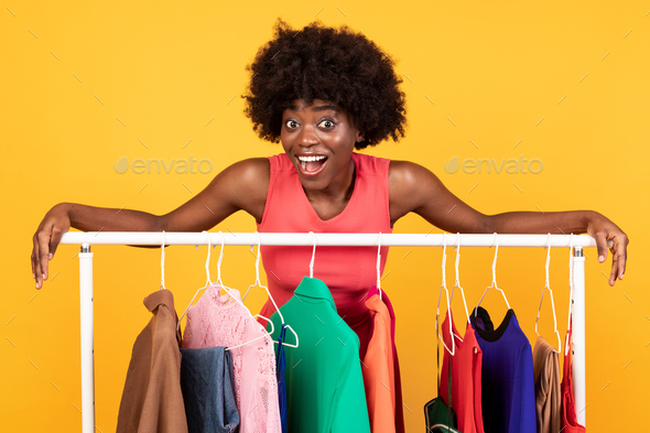 Excited Black Shopaholic Lady Posing Near Clothing Rack, Studio Shot