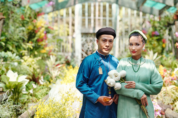 Man and woman in ao dai dresses and headwear - Stock Photo - Images