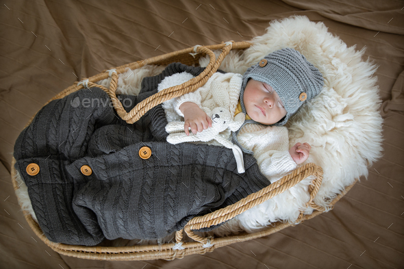 The baby sleeps sweetly in a wicker cradle in a warm knitted hat. - Stock Photo - Images
