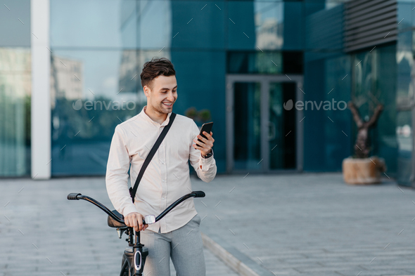 Outdoor portrait of handsome young man with mobile phone and bicycle in street