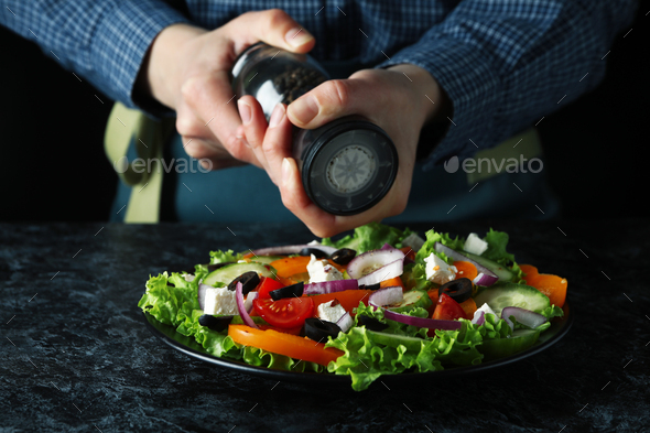 Woman grinding pepper on greek salad on black smokey table