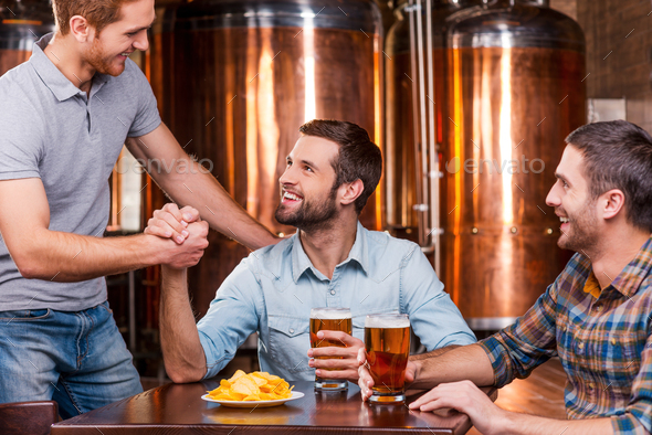 Meeting old friend. Three happy young men sitting in beer pub together while two of them handshaking
