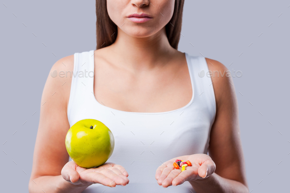 Make your choice! Cropped picture of young woman holding an apple and pills in her hands