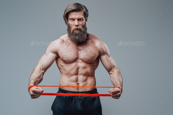 Muscular guy stretching rubber resistance bands in gray background