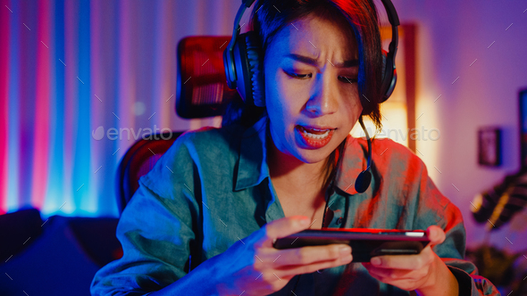 Happy asia girl gamer wear headphone competition play video game online  with smartphone. Stock Photo by Tirachard