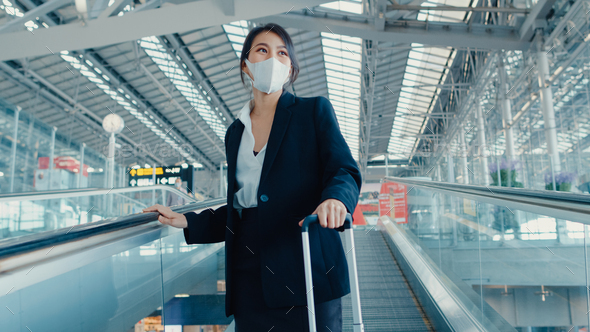 Asian business girl wear face mask drag luggage stand on escalator look around walk to terminal.