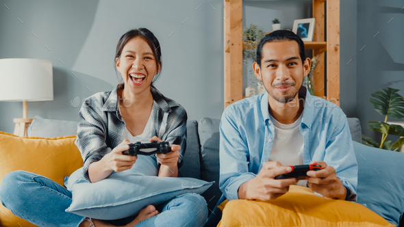 asia young couple man and woman sit on couch use joystick controller play video game.