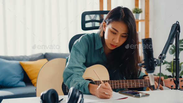 woman songwriter play acoustic guitar listen song from smartphone think and write notes.