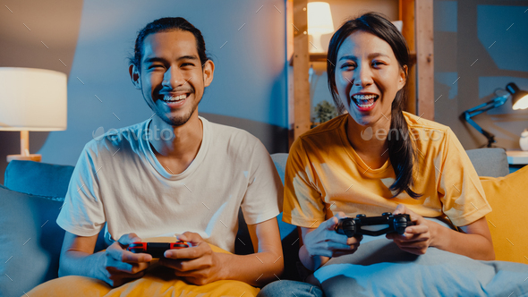 asia young couple man and woman sit couch use joystick controller play video game spend fun time.