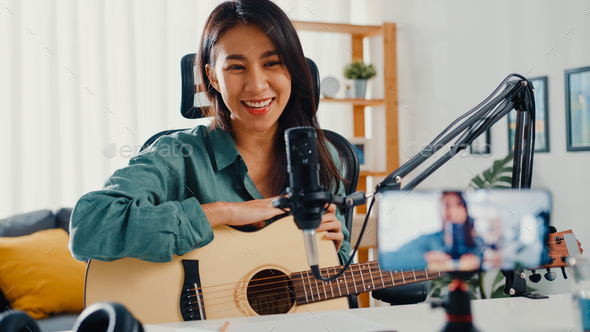 Asia girl influencer play guitar music use microphone record with smartphone for online.