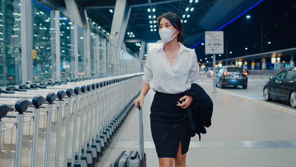girl arrive destination wear face mask with drag luggage walk outside wait car terminal.