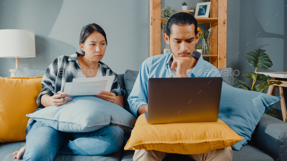 man and woman sit on couch serious focus on laptop computer check document paper pay bills.