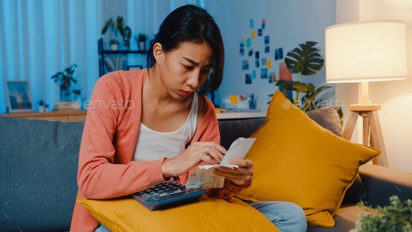 Asian lady feel stress and worried with bill and invoice credit card calculating loan on sofa.