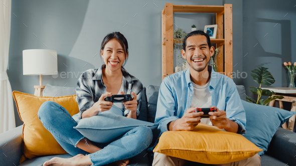 man and woman sit on couch use joystick controller play video game spend fun time together.