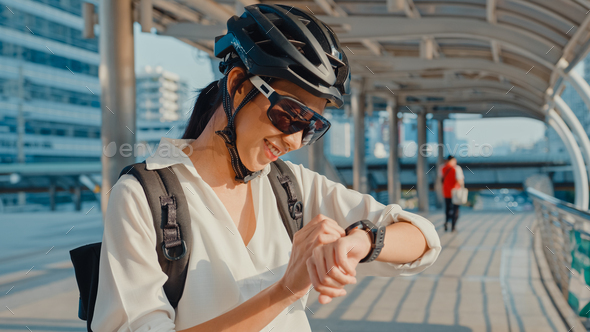 Asian businesswoman with backpack bicycle look smartwatch in city street go to work at office.