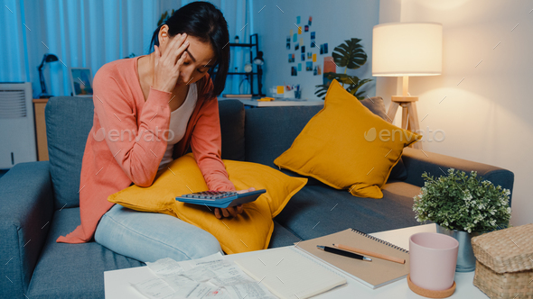 Asian lady feel stress and worried with bill and invoice credit card on sofa at home.