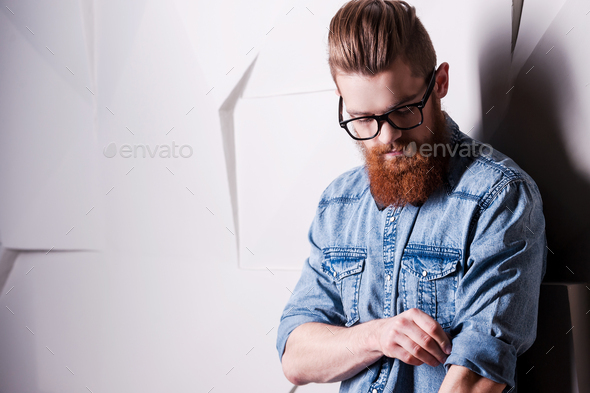 Being attentive the small details. Handsome young bearded man wearing glasses and rolling up sleeves
