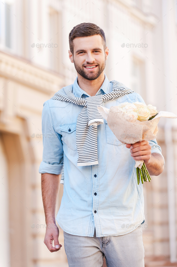 This is for you! Handsome young man holding bouquet of flowers while walking by the street