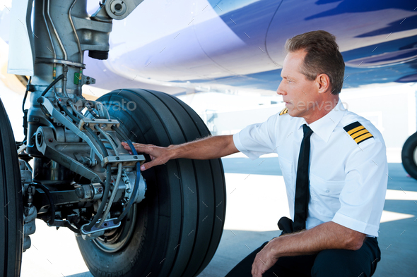 Checking the wheels. Confident male pilot in uniform examining an airplane wheels