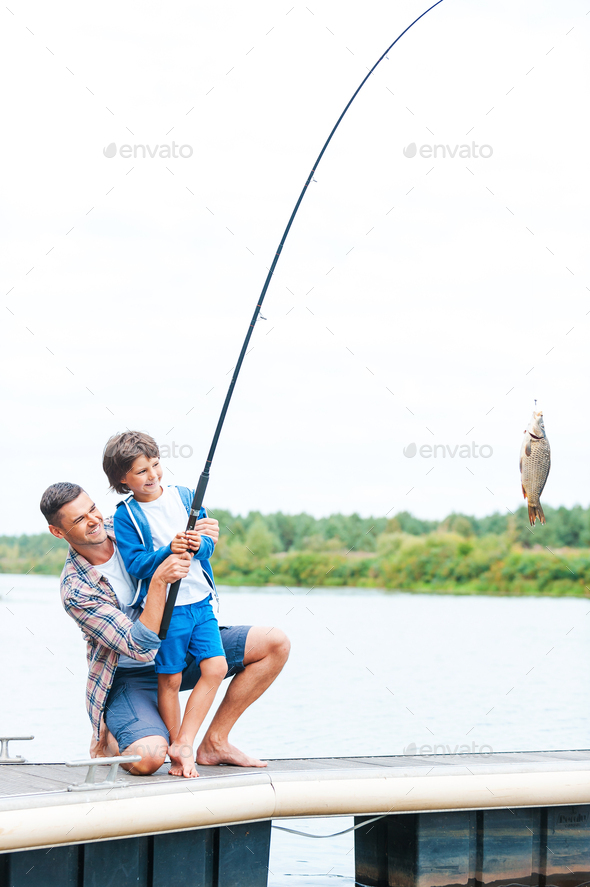 It is a big fish! Father and son stretching a fishing rod with fish on the hook