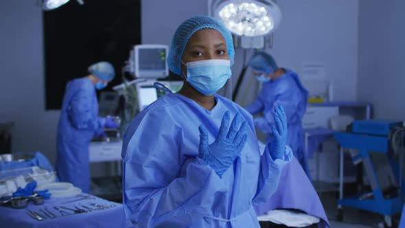 African american female surgeon wearing face mask and protective clothing in operating theatre alt