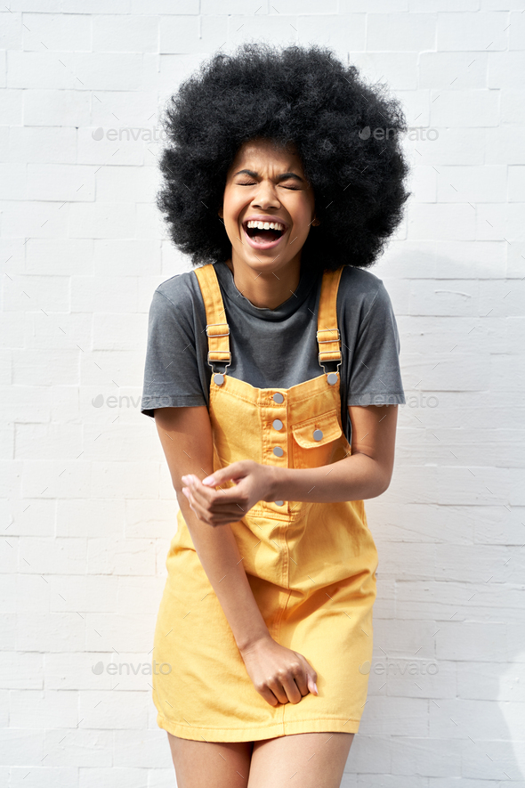 Funny African lady with Afro hair laughing standing against white brick  wall. Stock Photo by insta_photos