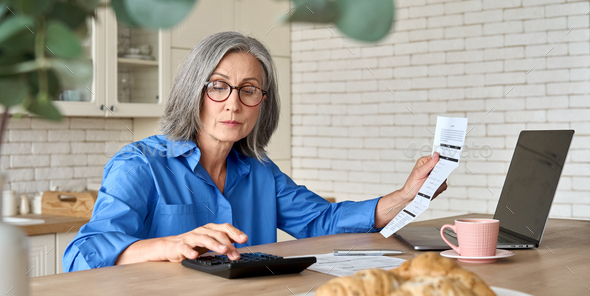 Senior mid 60s aged woman calculating bank fee with computer. - Stock Photo - Images