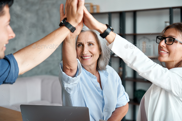 Happy old female mentor give high five to young employees students team. Stock Photo by insta_photos