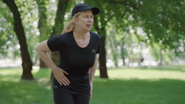 Middle Shot of Mid-adult Woman Suffering Stomach Cramps After Jogging in Summer Park. Portrait of alt