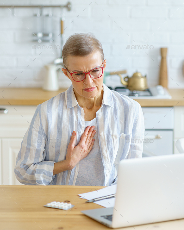 Middle aged woman explaining symptoms to doctor online while sitting in kitchen at home - Stock Photo - Images