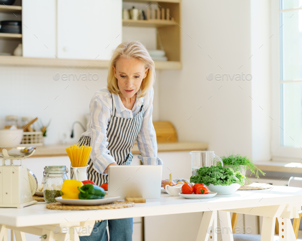 Eldrely female watching online culinary class or video recipes while cooking at home in modern - Stock Photo - Images