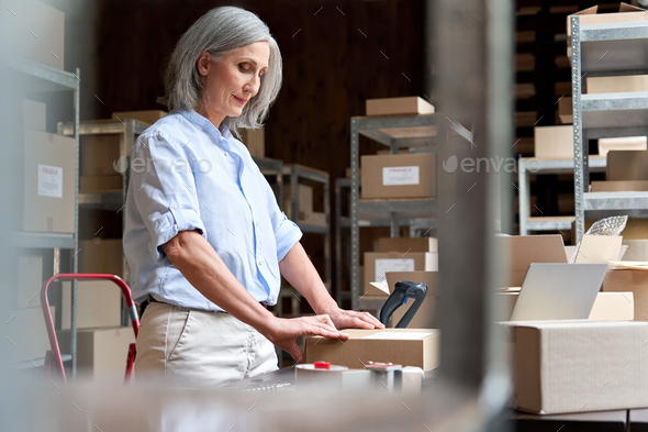 Mature female online store business owner packing parcel shipping box.