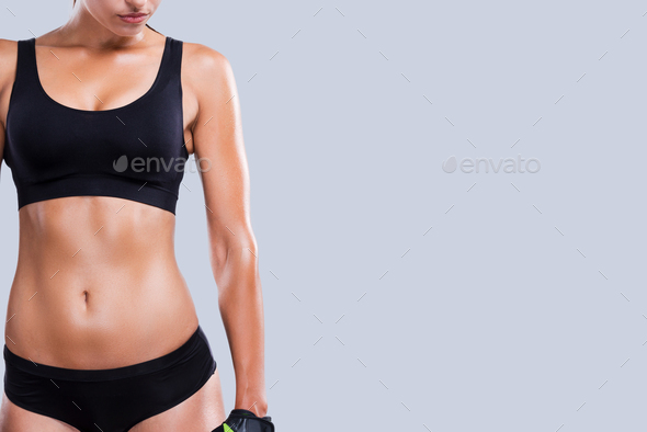 Perfect curves. Close-up of young sporty woman with perfect body standing against grey background