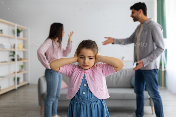 Childhood traumas concept. Upset arab girl covering ears with hands not to listen parents conflict