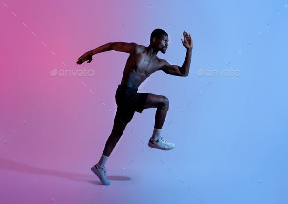 Full length of strong black athlete in sportswear running in neon light,  side view. Active lifestyle Stock Photo by Prostock-studio