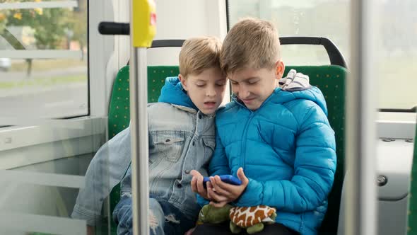 Two Boys In The Passenger Seat On The Bus Playing Smartphones alt