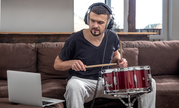 A young man with headphones learns to play the drum using online lessons.