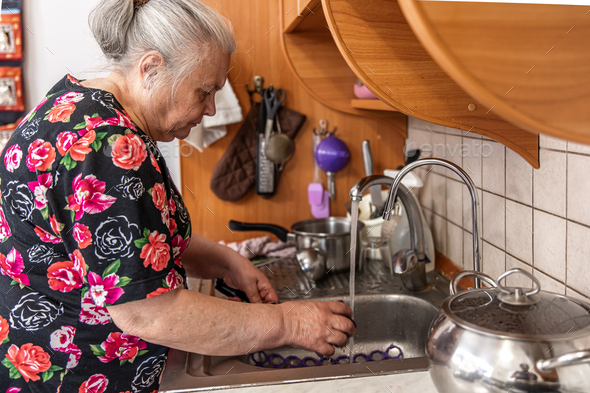 A woman aged in a dressing gown washes the dishes.