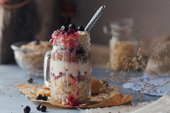Layered dessert with muesli, yogurt, banana and berries in glass mason jar - Stock Photo - Images