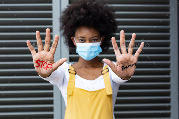 Portrait of mixed race woman wearing face mask making stop gesture with hands covered in writing