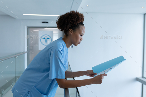 African american female doctor standing in hospital corridor looking at medical documentation