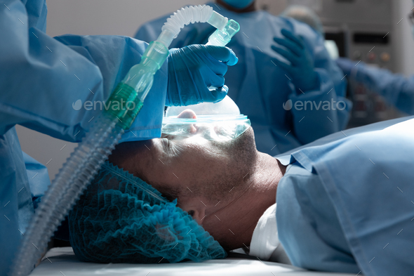 Caucasian male patient lying on surgical bed wearing oxygen mask in operating theatre