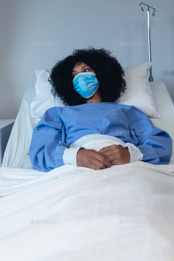 African american female patient lying in hospital bed wearing face mask