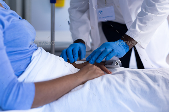 Midsection of african american male doctor preparing iv tube of female patient in hospital bed - Stock Photo - Images
