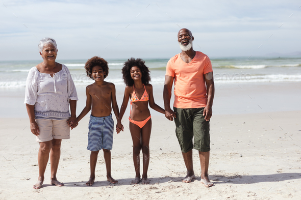 Portrait of african american grandparents and grandchildren holding hands smiling at the beach